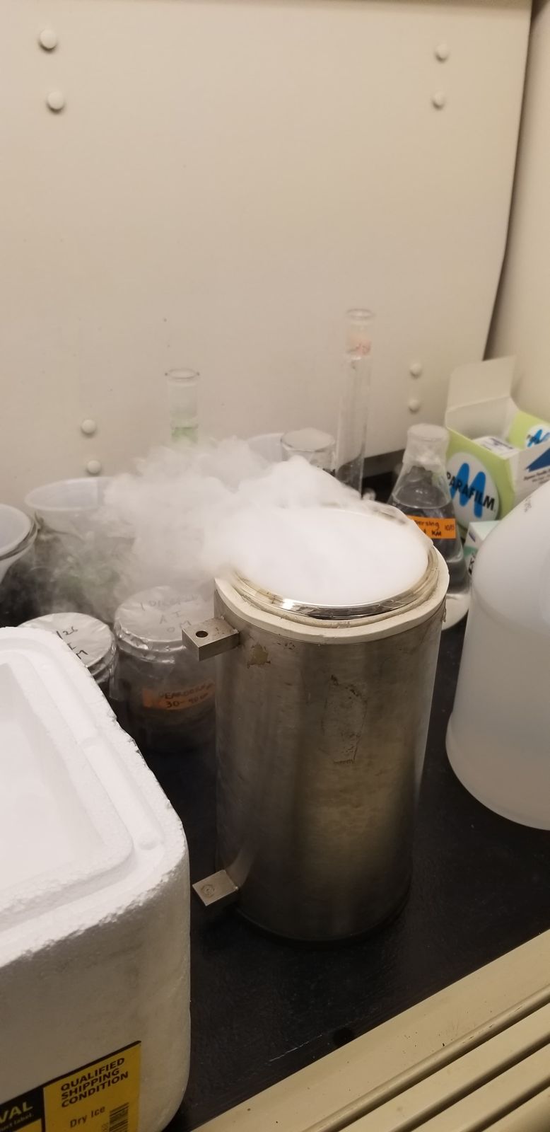 Stainless steel cylinder fogging over with a dry ice slurry, with soil sample jars beside it in a fume hood.